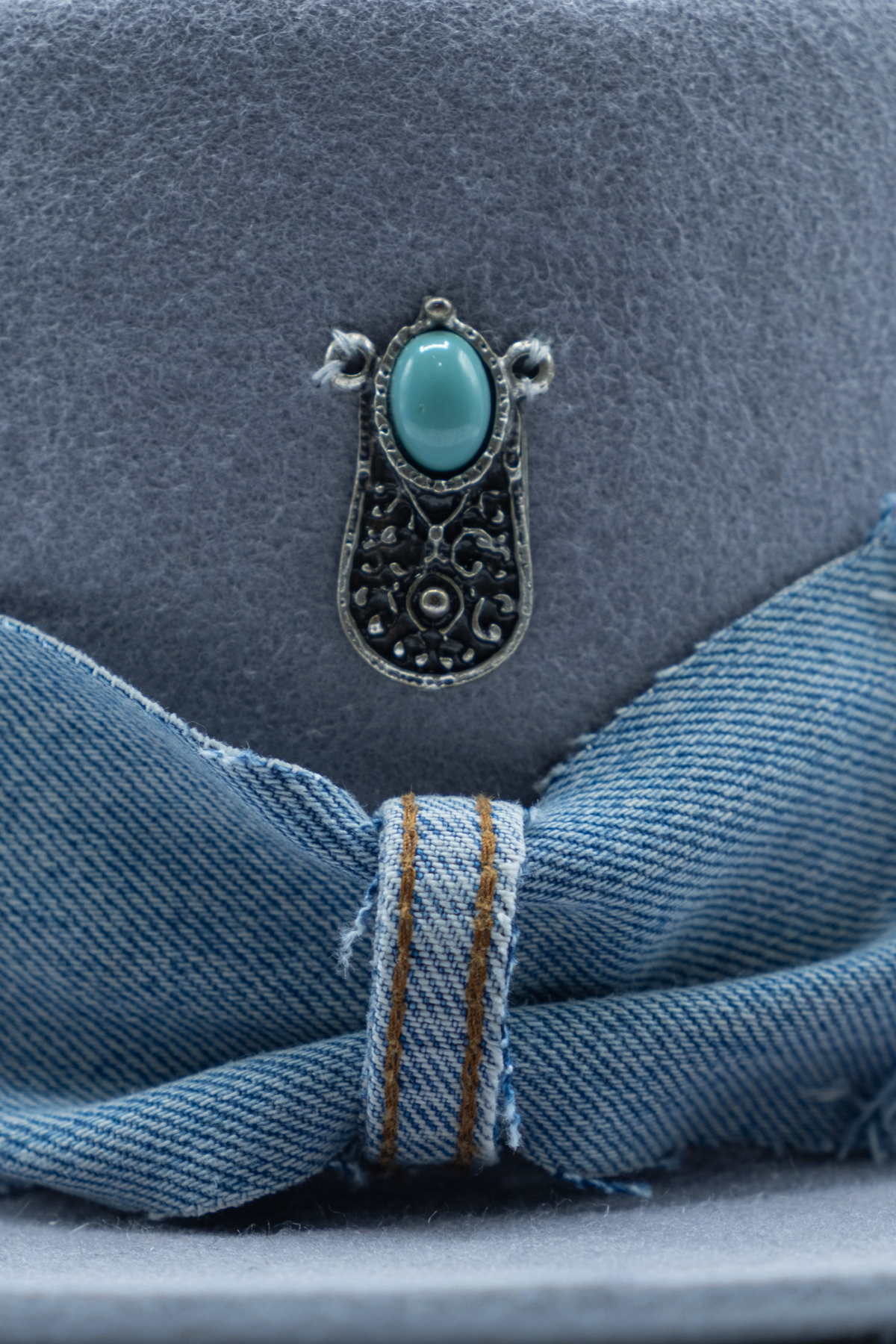 Dettaglio del fiocco sfrangiato effetto denim e dell'ornamento color argento con elemento turchese di Polvo Sam